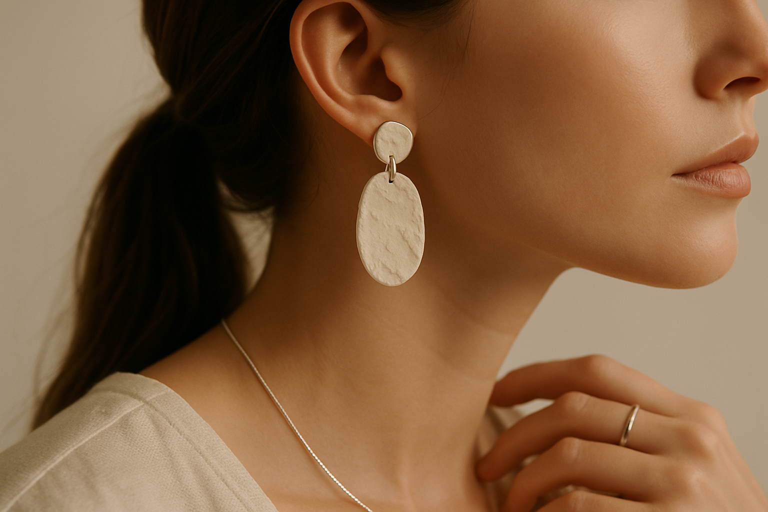 Close-up photo of a woman wearing handmade clay earrings and silver jewelry, shot from the side or back, with her face not visible. Aesthetic and minimalistic composition, soft natural lighting, neutral background in beige tones. Fashion editorial style